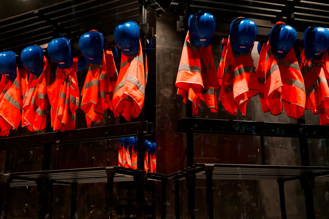 who-we-are Row of orange safety vests and blue helmets hanging in industrial setting