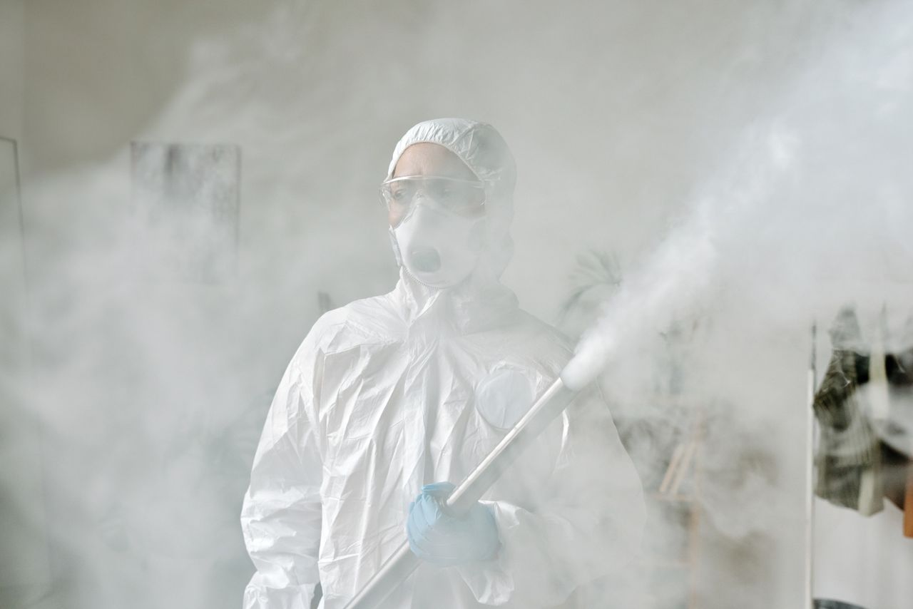 services-01 Person in protective gear fumigating an area indoors amid smoke for disinfection.