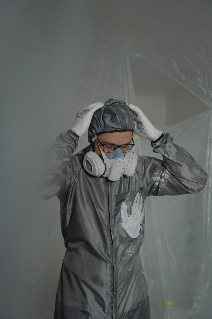 A worker wearing a gas mask and protective suit stands indoors, focusing on safety.