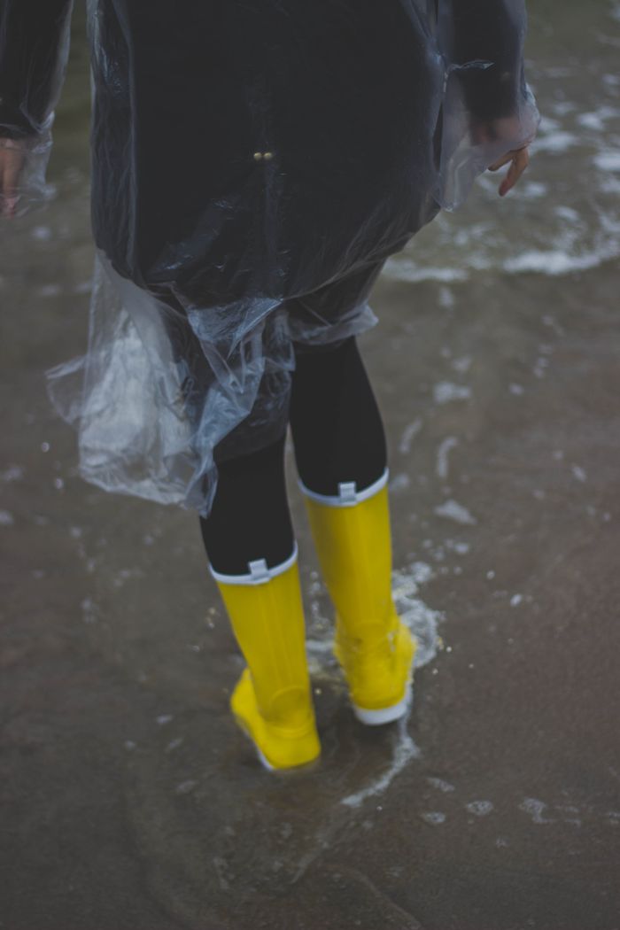 team-04 Person wearing yellow boots and raincoat, splashing through water outdoors.