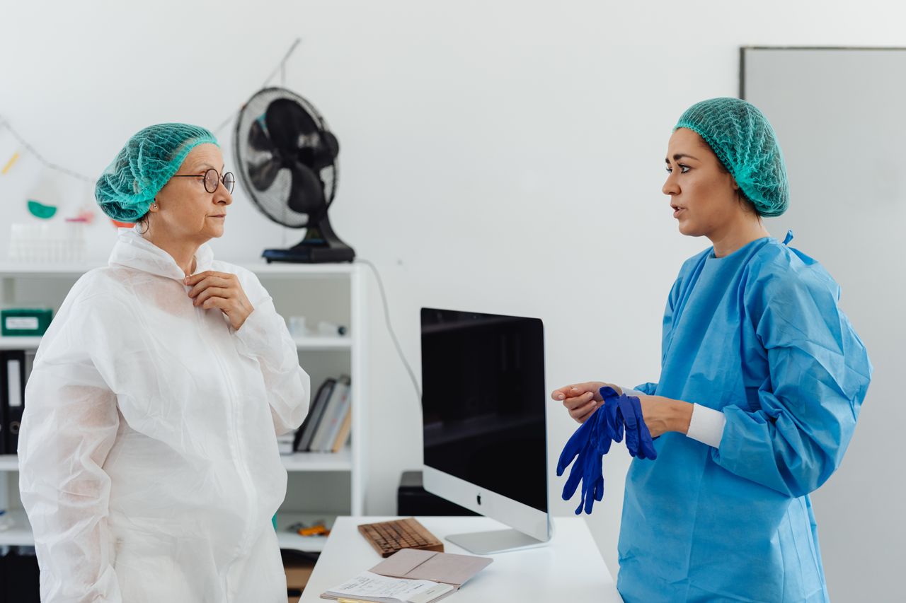 services-02 Two female healthcare professionals in conversation wearing protective gear in a laboratory setting.